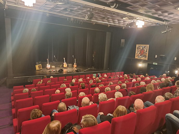 Ett gäng seniorer sitter i en konsertlokal och väntar på att en konsert ska börja